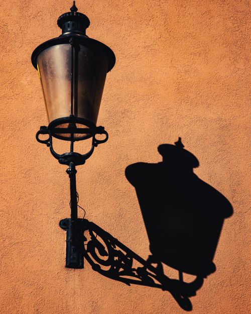 Free Artistic shot of a vintage street lamp casting a shadow on a sunlit orange wall. Stock Photo