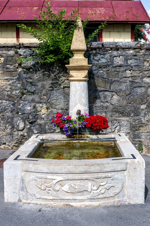 Free An ornate stone fountain adorned with bright flowers set against a textured stone wall. Stock Photo