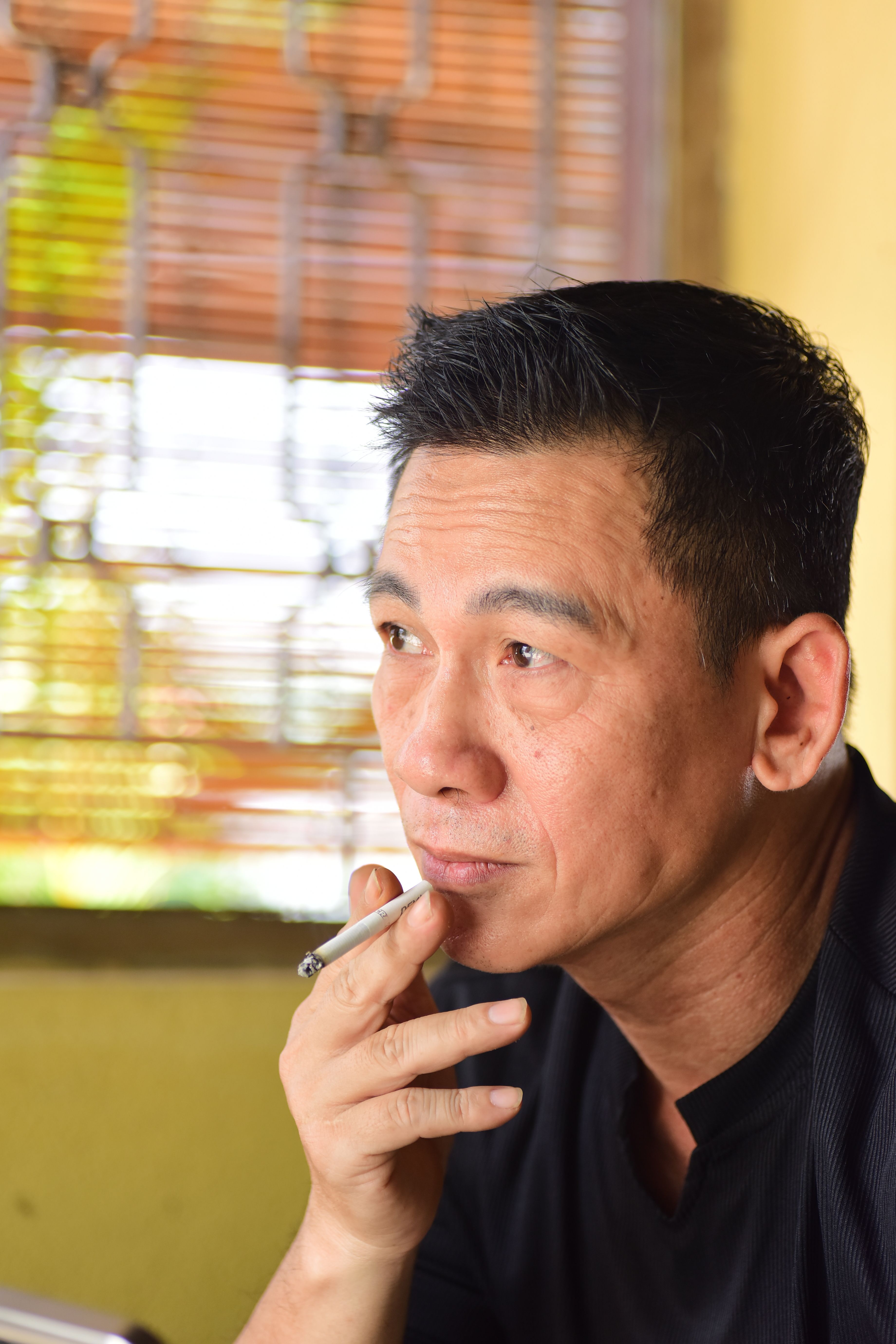 Middle-aged man in thoughtful pose, holding a cigarette indoors, near window.