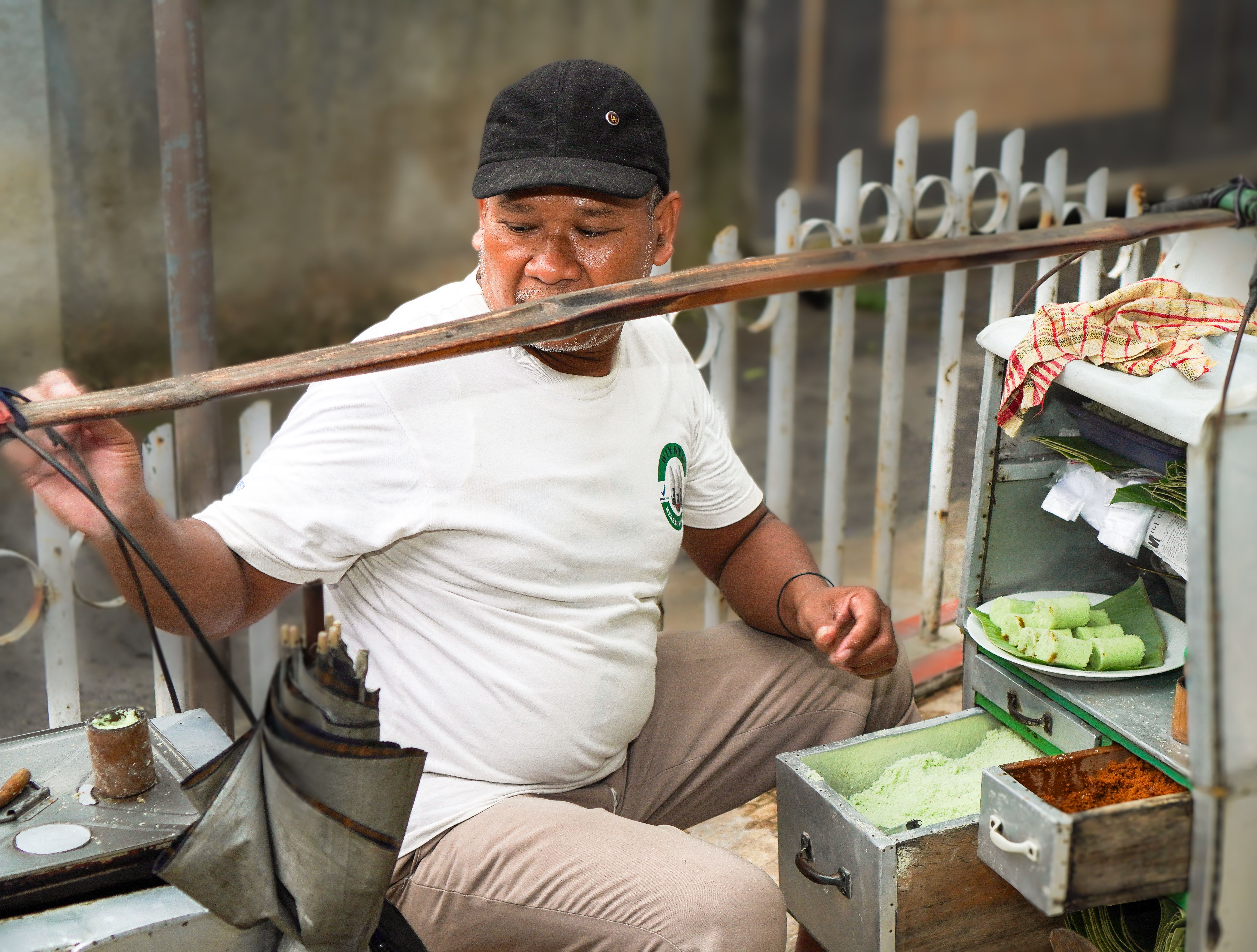 Local street vendor preparing traditional snack with green rice cakes outdoors.