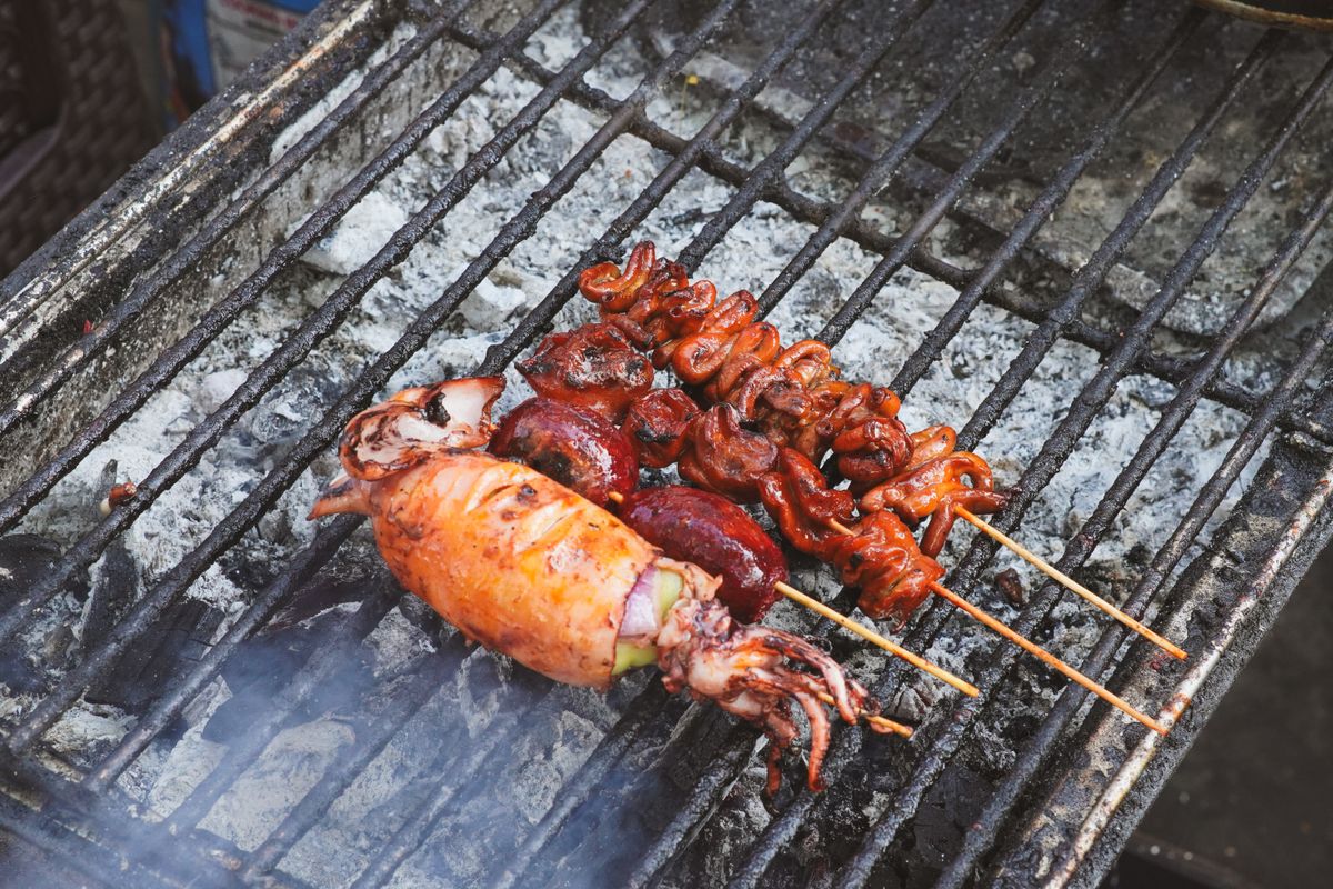 Whole squid and glazed squid pieces on bamboo skewers grilling over glowing charcoal