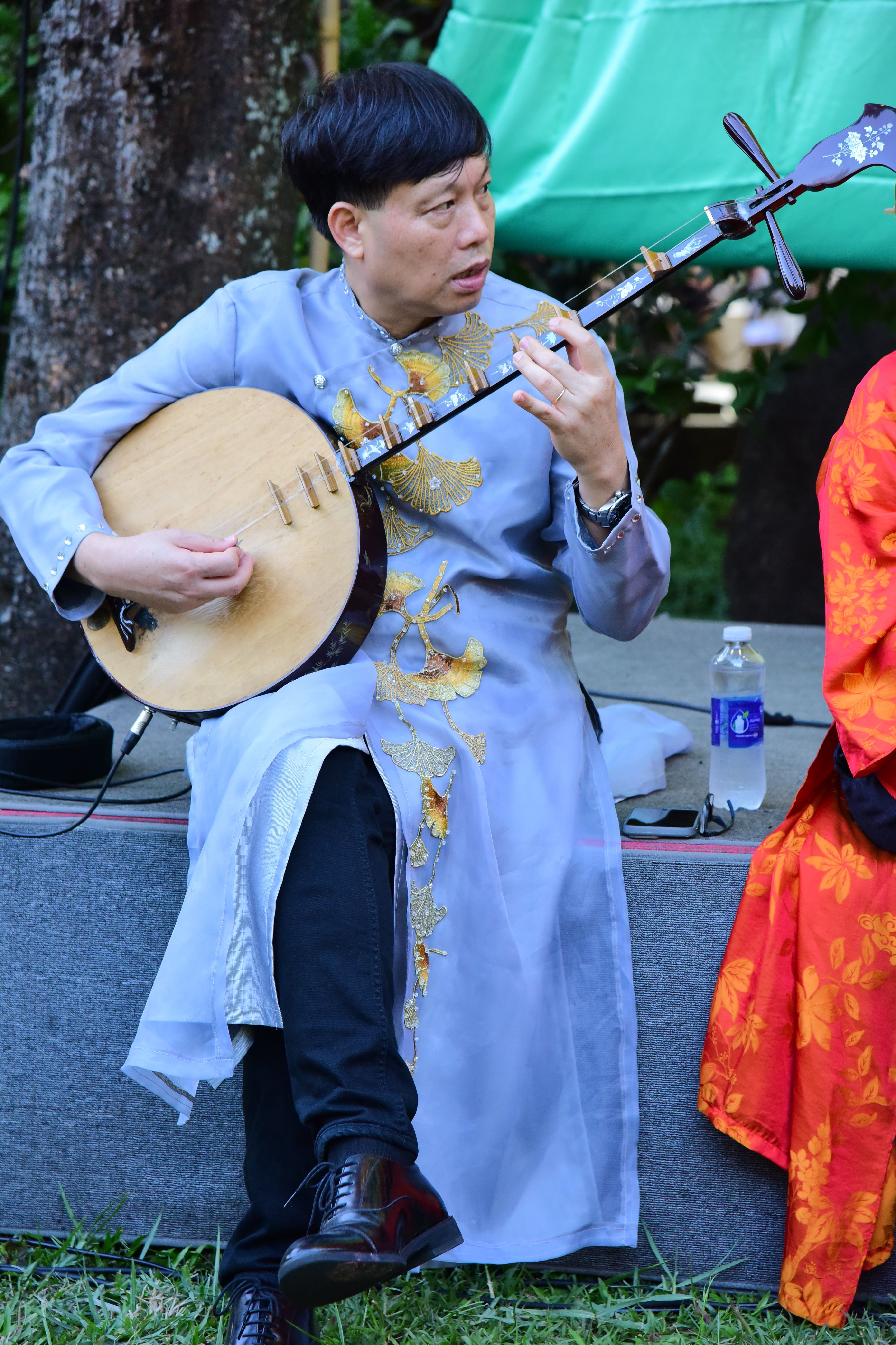 A musician in traditional attire plays the Vietnamese Dan Nguyet lute outdoors.