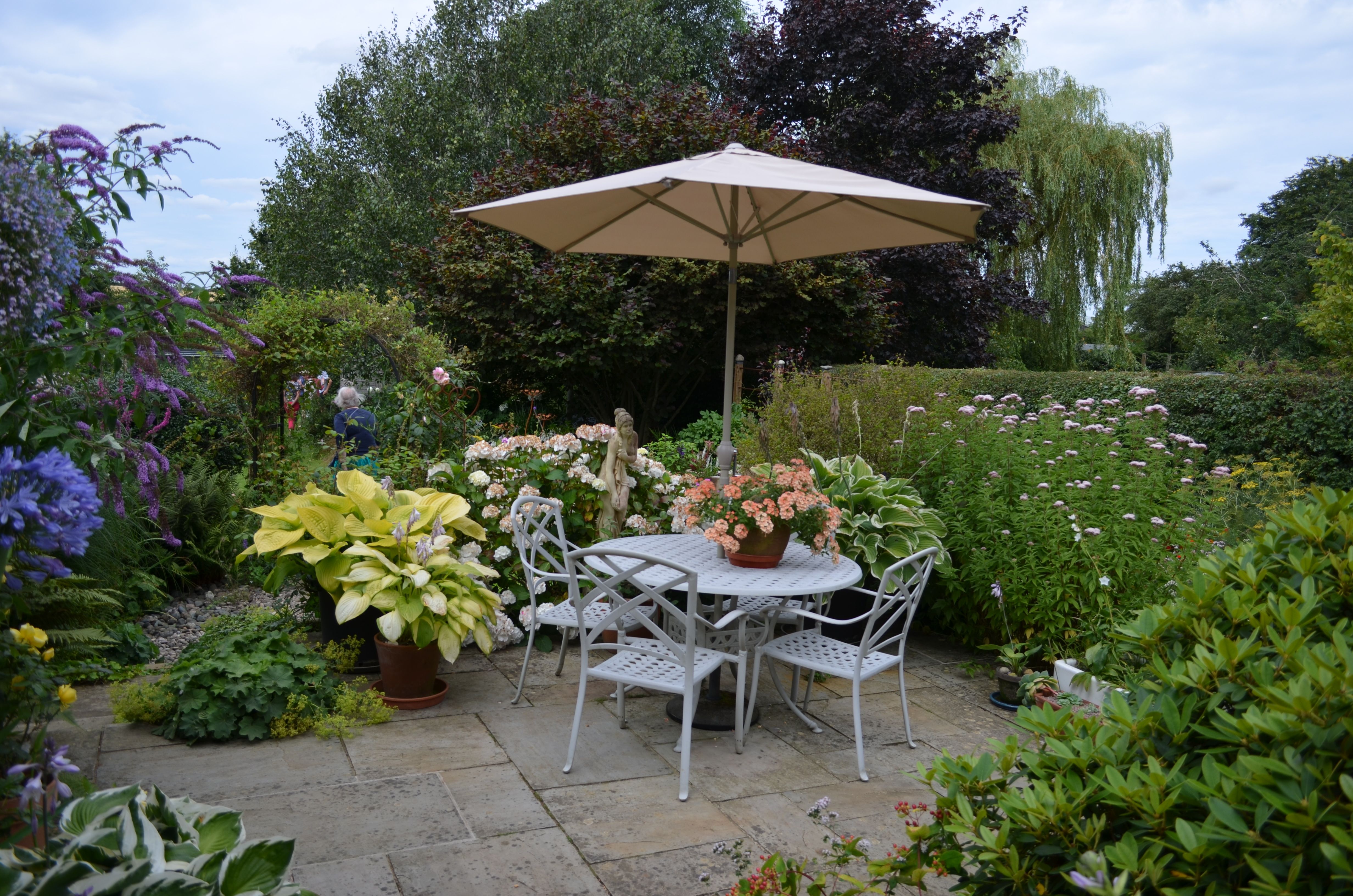 A serene garden patio featuring a table with chairs, umbrella, and vibrant flowers in full bloom.
