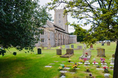Free A picturesque view of a historic church and cemetery surrounded by lush greenery in an English countryside. Stock Photo
