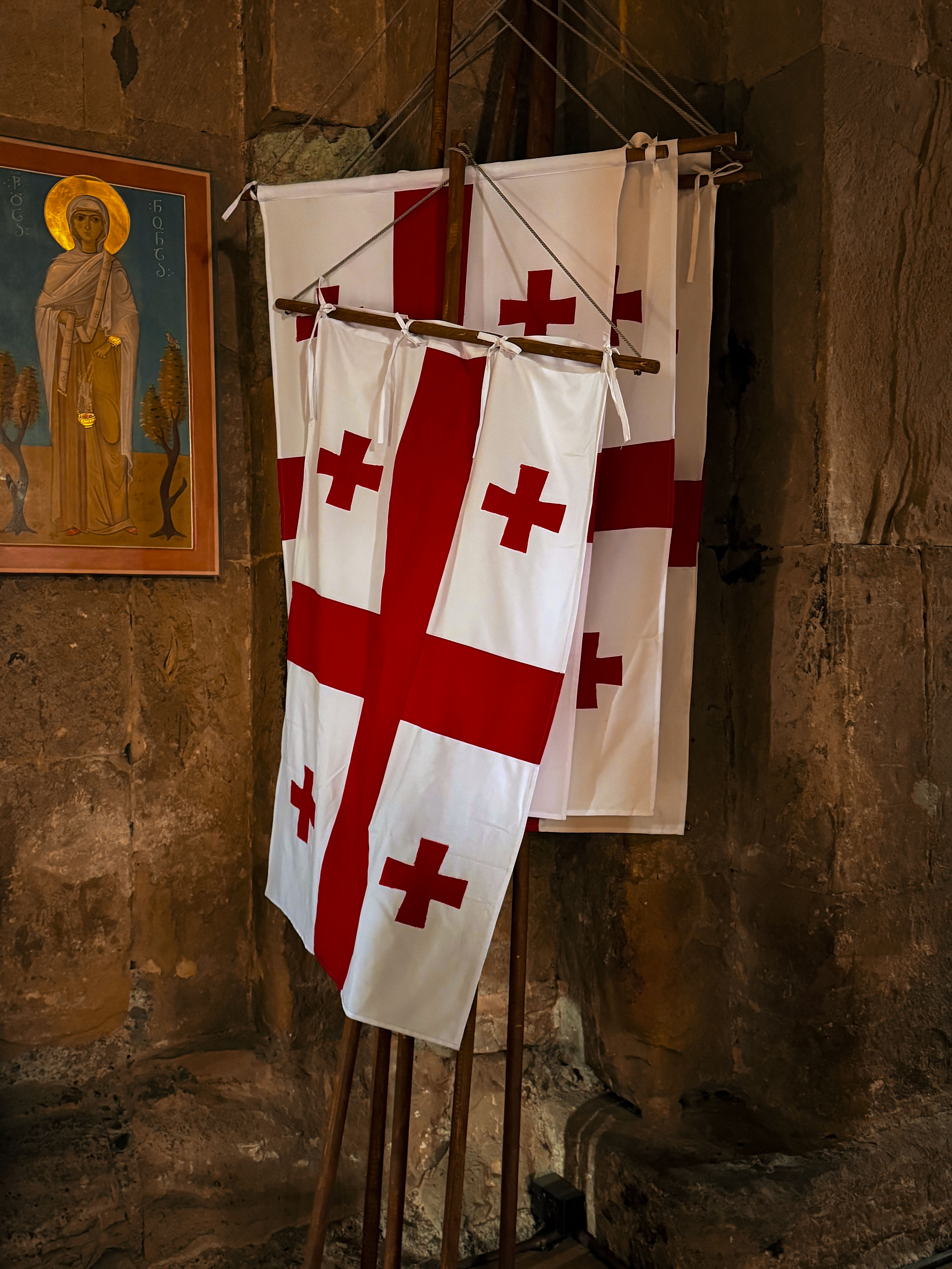 Flags of Georgia displayed inside a historic church with religious iconography. Cultural heritage ambiance.
