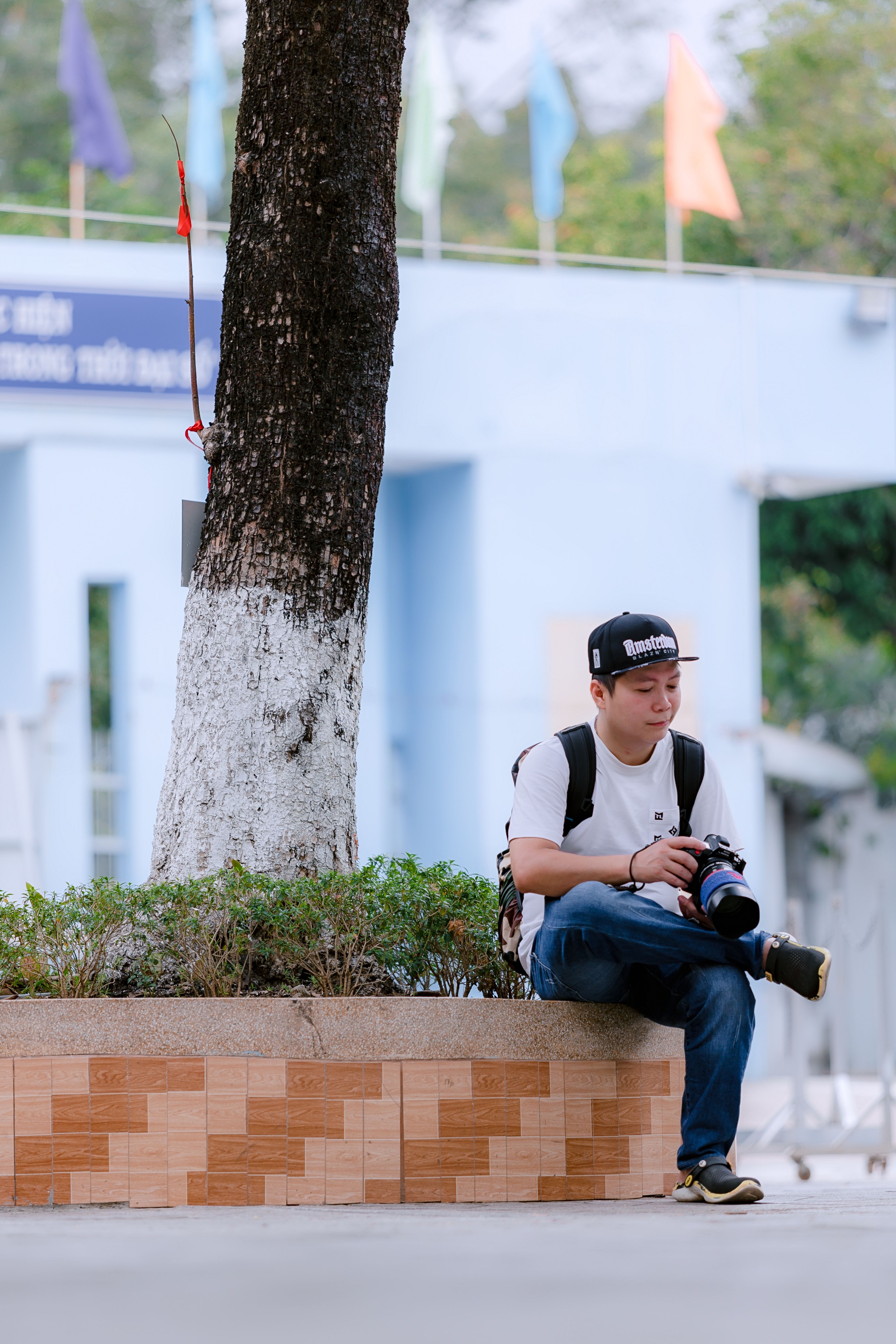 A young photographer relaxes with camera outdoors, capturing urban life.