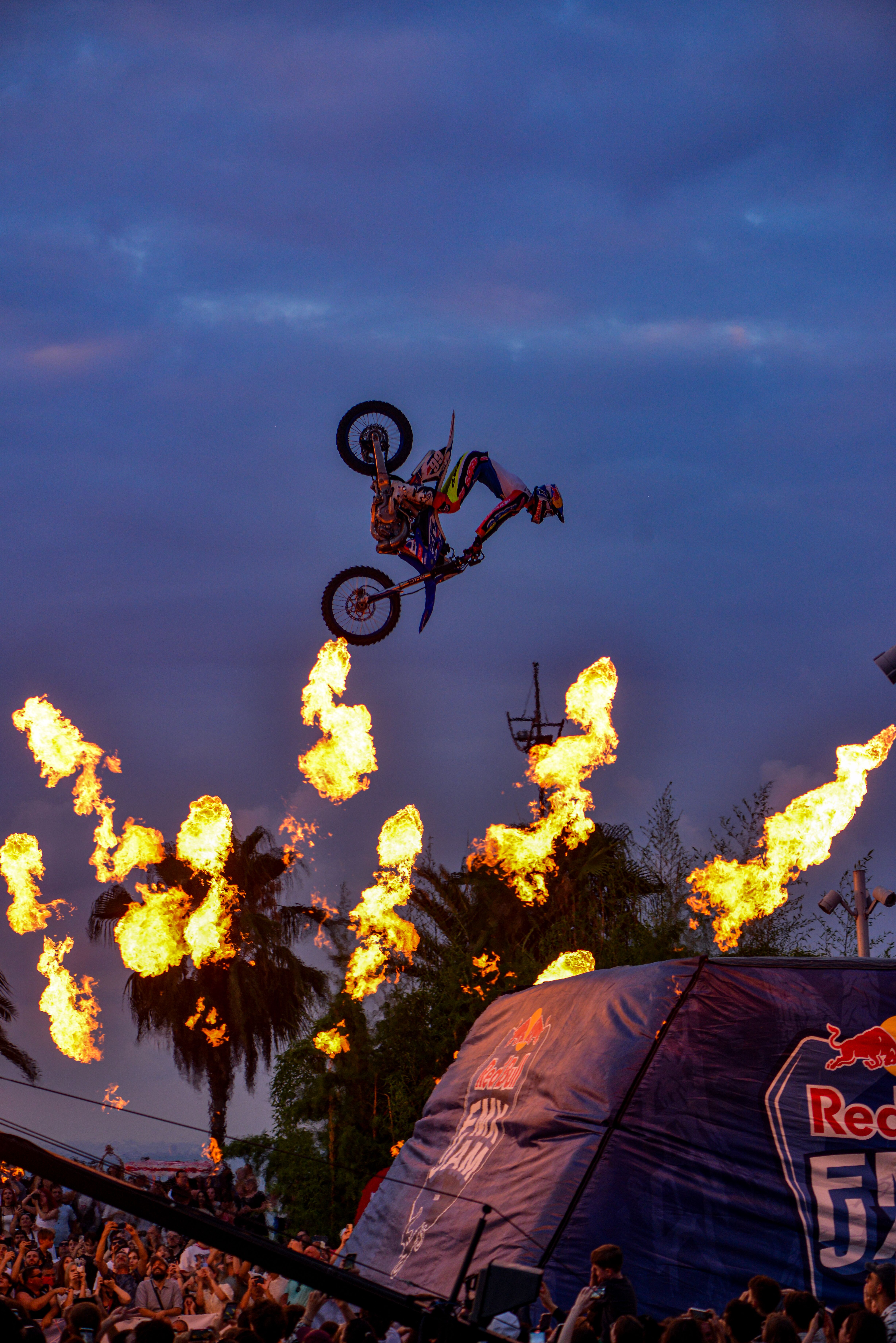 A breathtaking motocross stunt with fire effects against a sunset sky.