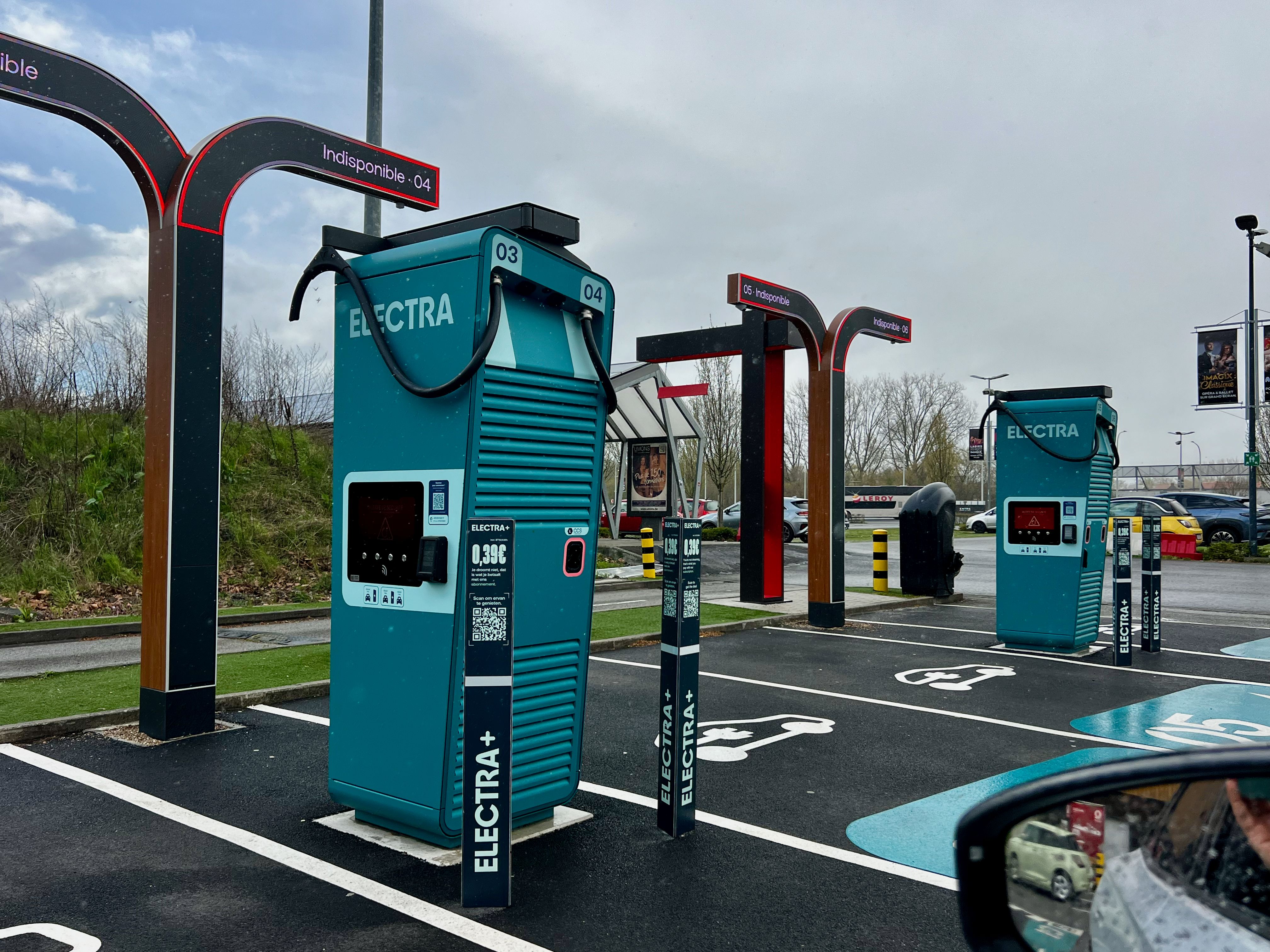 A modern electric vehicle charging station in a parking lot on a cloudy day.
