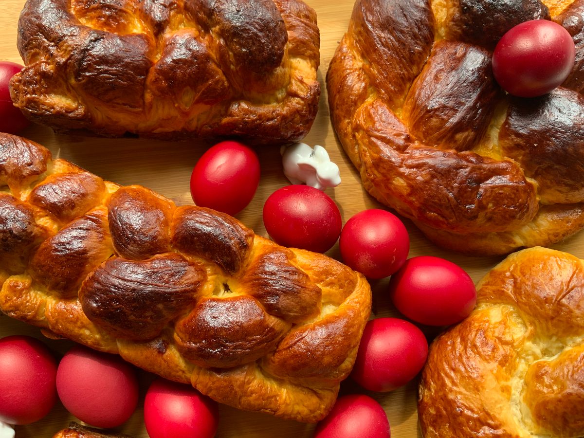 Several dark glossy braided tsoureki loaves surrounded by bright red dyed Easter eggs