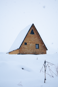 A solitary wooden cabin covered in snow, illustrating a serene winter scene.