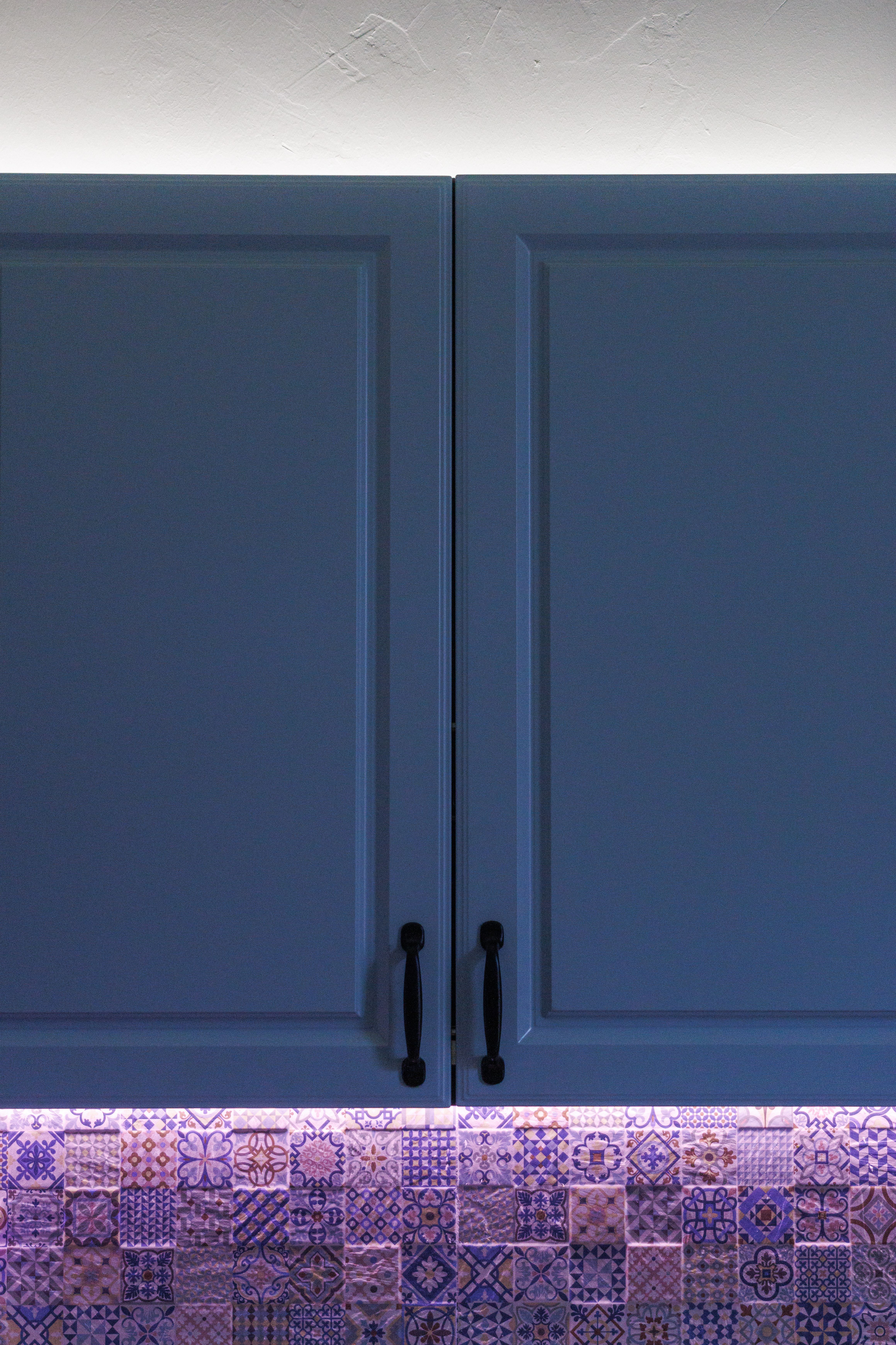Stylish kitchen featuring blue cabinets and decorative tiles with under-cabinet lighting.