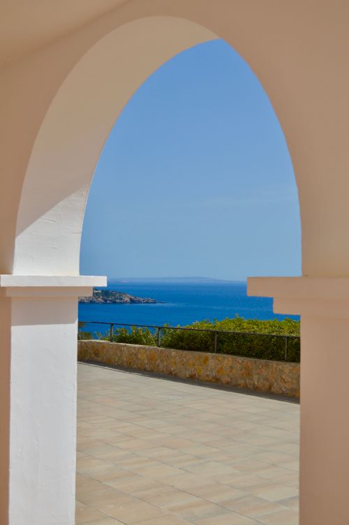 Free A beautiful seaside with blue waters seen through an elegant white archway under a clear sky. Stock Photo