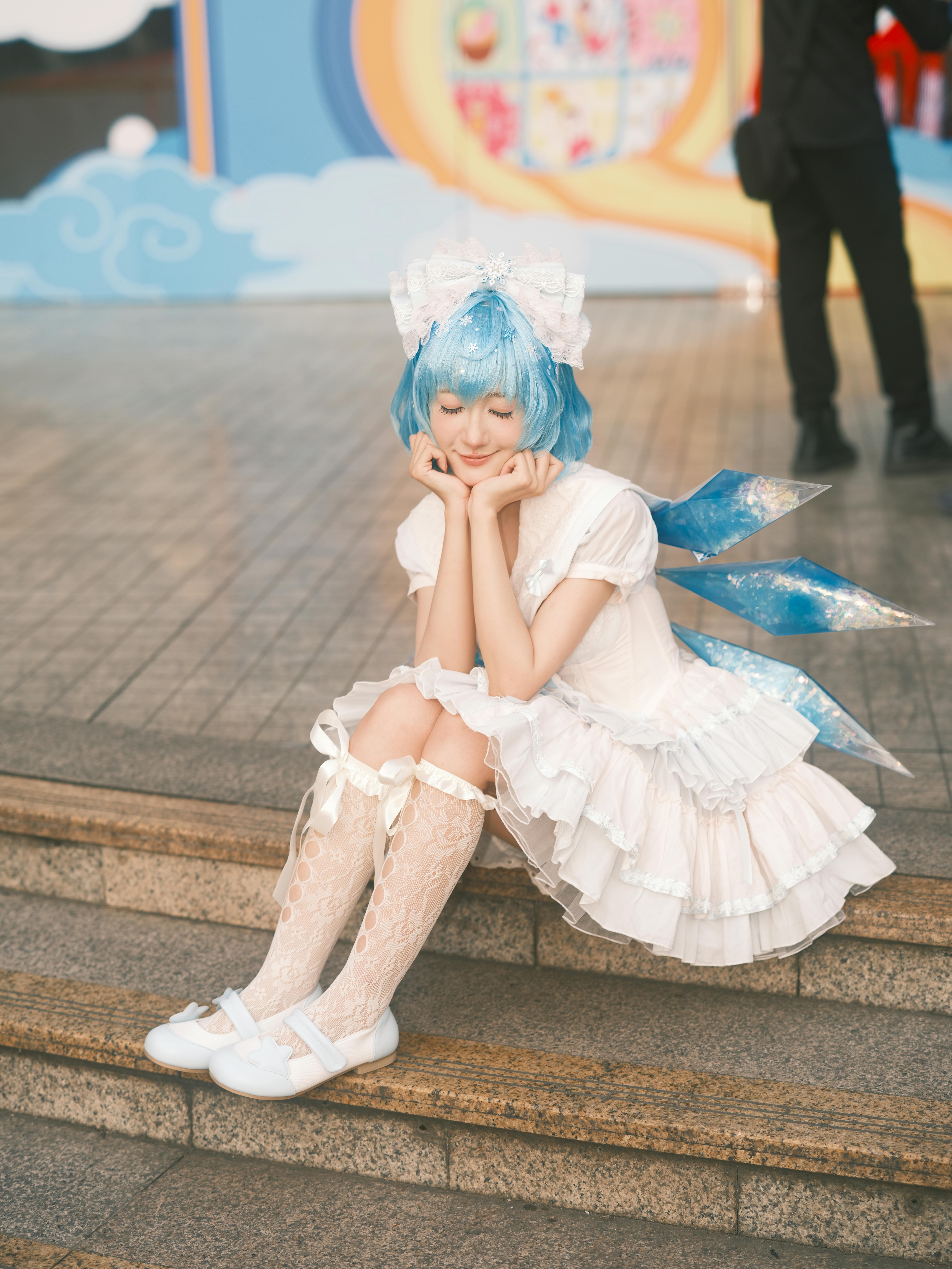 Young woman in anime cosplay with blue wig, sitting on steps, captures fantasy vibe in Vietnam.