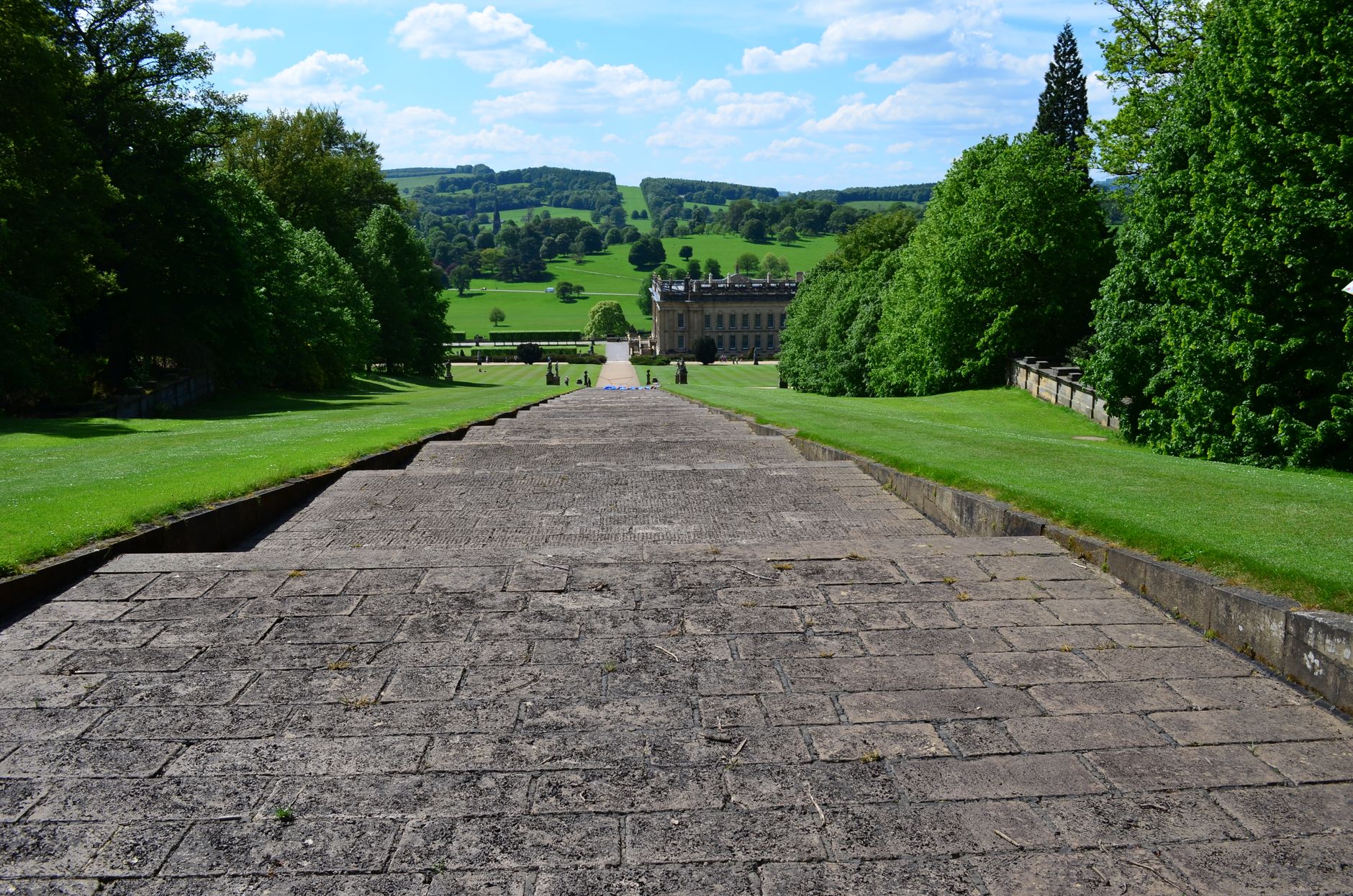 Wide-angle view of Chatsworth House garden path with manicured lawns and the Derbyshire hills beyond