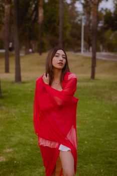 A woman in a red shawl standing in a vibrant park setting, exuding confidence.