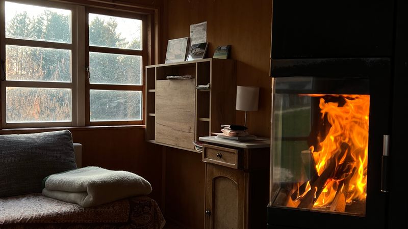 A small timber room with a lit wood burner and a window seat