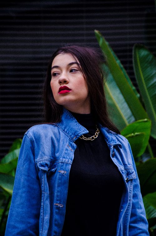 Free Stylish woman in denim jacket against lush green tropical plants Stock Photo
