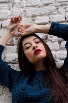 Fashionable young woman in a teal sweater poses against a white brick wall, exuding confidence and style.