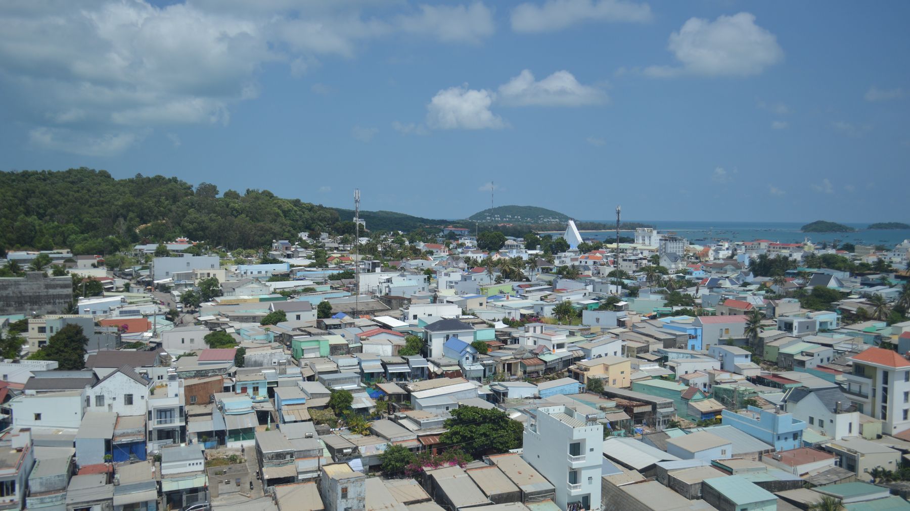 A scenic aerial view of a coastal city with colorful buildings and ocean in the background under a blue sky.