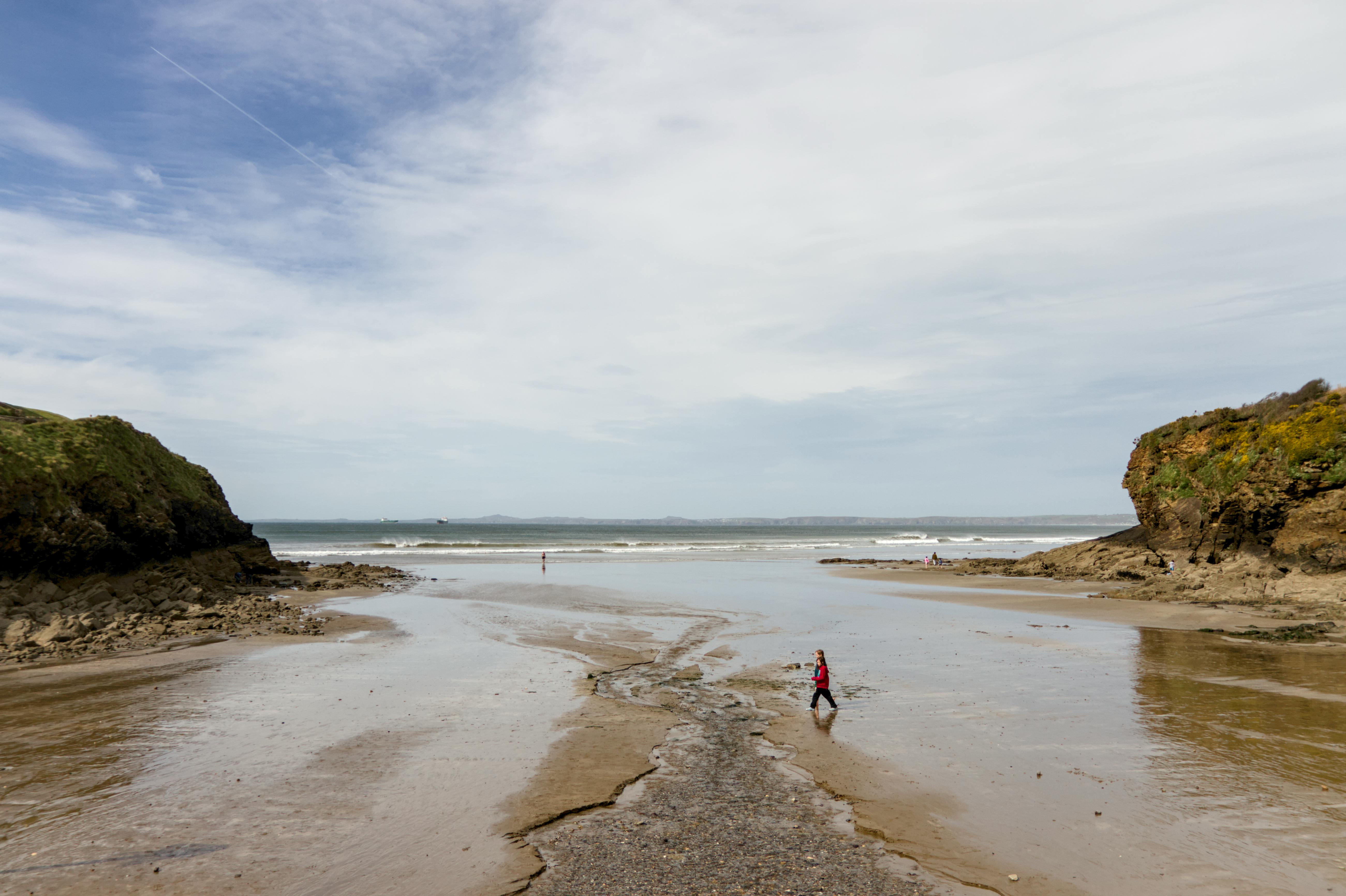 A picturesque Welsh beach with cliffs and ocean, featuring a lone person walking by the shore on a sunny day.