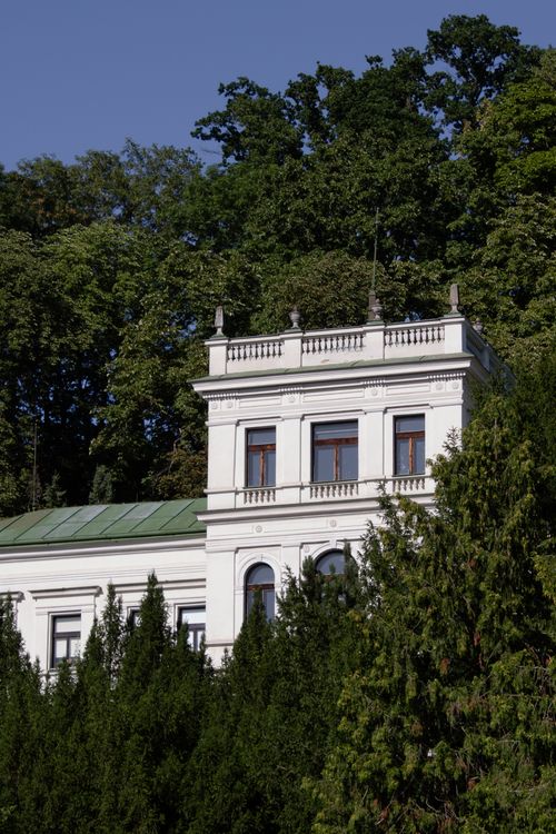 Free A majestic white building set against a backdrop of dense green trees, exuding a serene and classical charm. Stock Photo