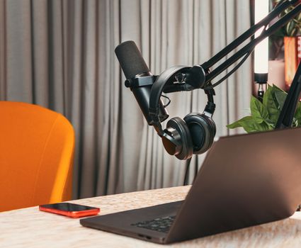 Modern podcasting studio with mic, headphones, laptop, and smartphone on a wooden table.