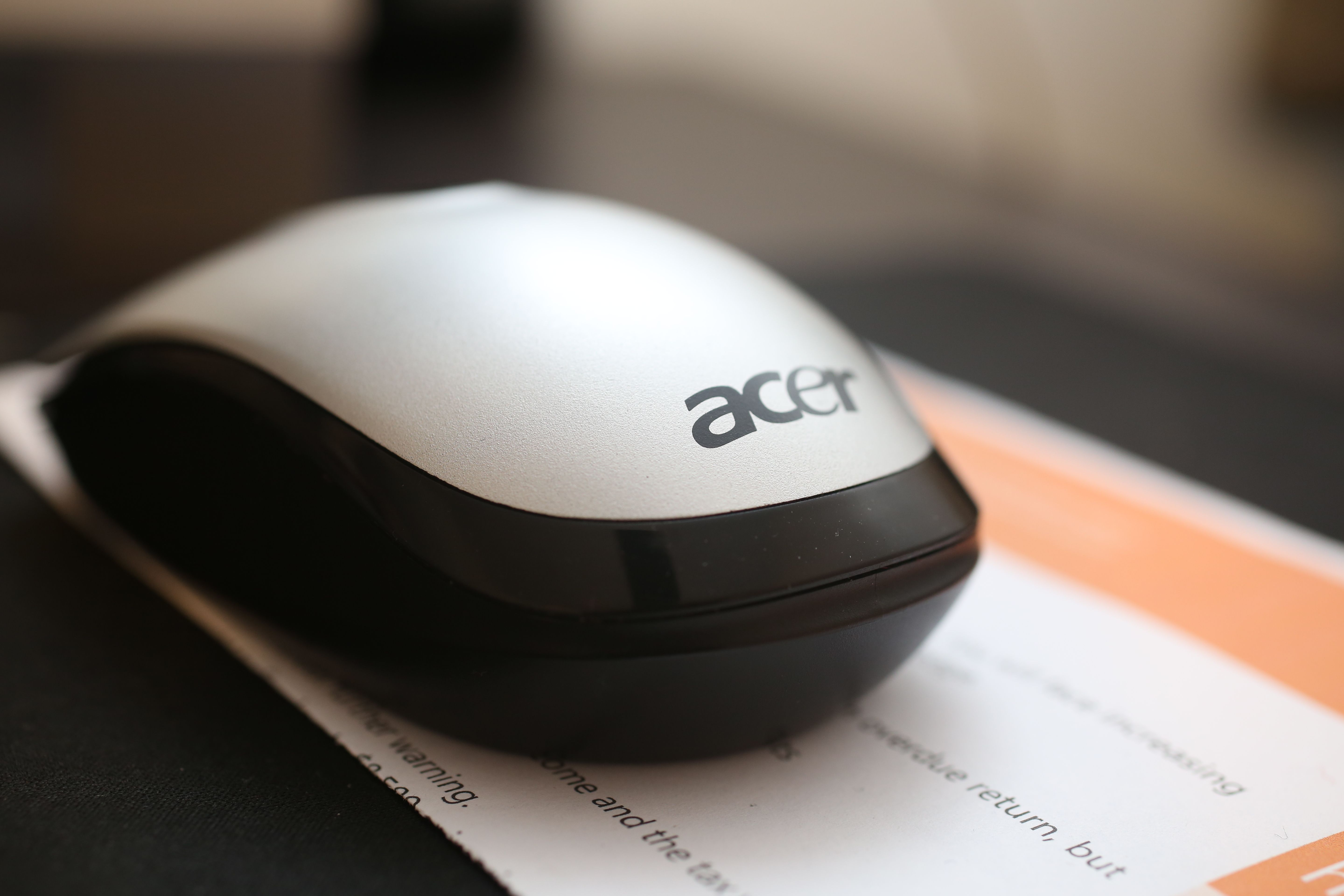 Detailed image of an Acer wireless mouse placed on a desk with blurred documents in the background.