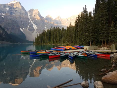 A serene view of canoes docked on Moraine Lake with majestic mountains in Alberta, Canada.