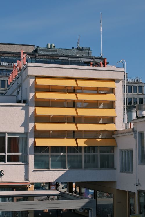 Free A modern urban building with prominent yellow awnings against a clear blue sky. Stock Photo