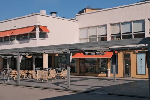 Free Sunny day at an outdoor cafe with modern architecture and empty seating area. Stock Photo