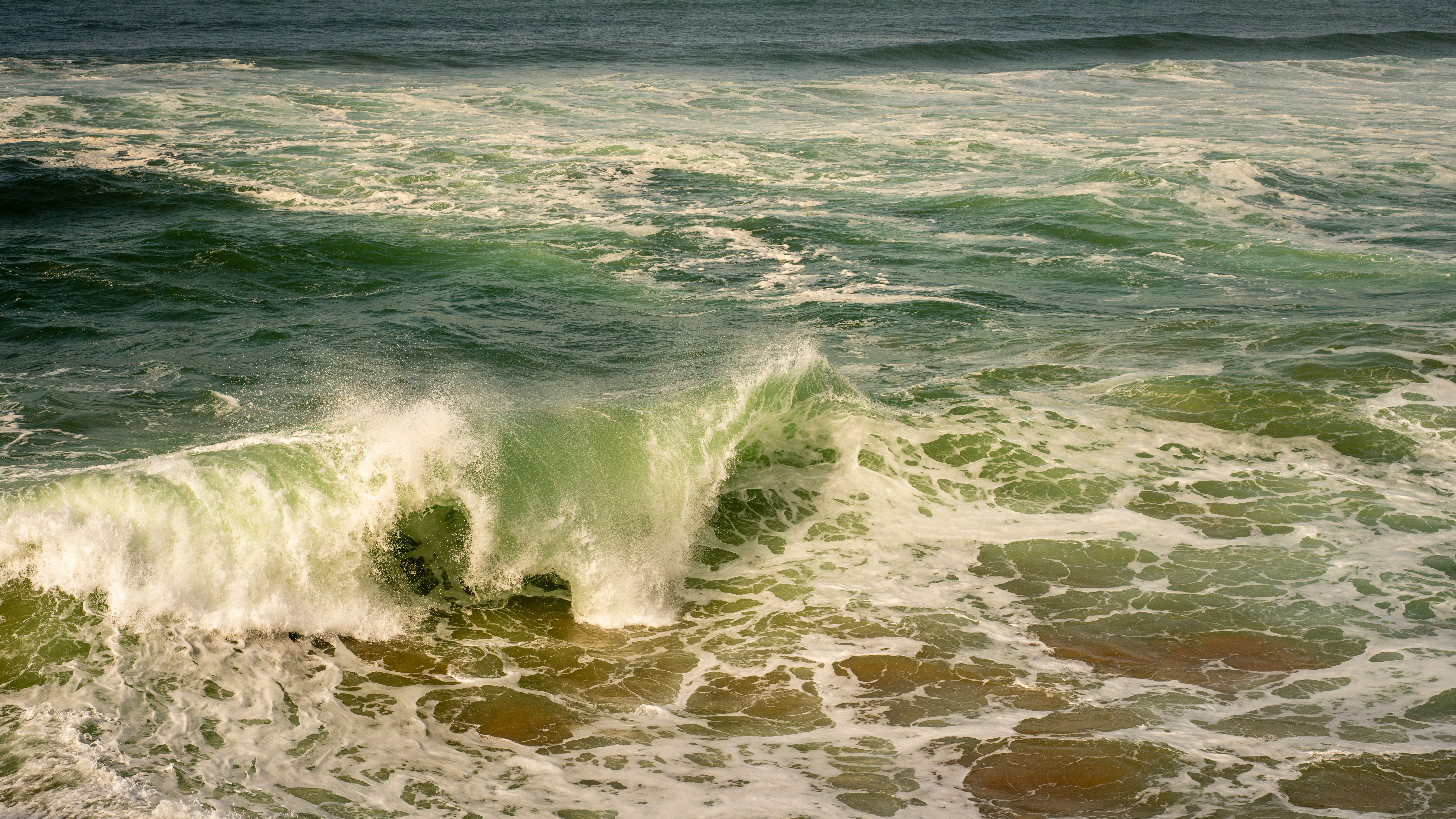 A stunning view of a powerful ocean wave crashing with green and blue hues in Cascais, Portugal.
