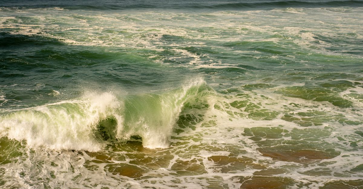 A stunning view of a powerful ocean wave crashing with green and blue hues in Cascais, Portugal.