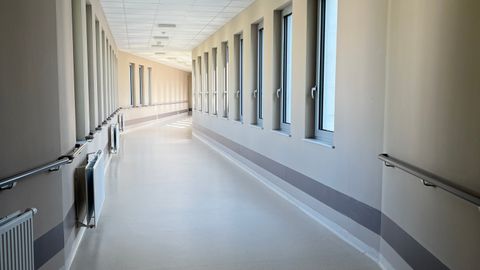 A modern, empty hospital corridor with large windows and handrails, well-lit and inviting.