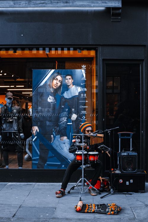 Free A street musician performs with drums outside a fashion store with vibrant posters. Stock Photo