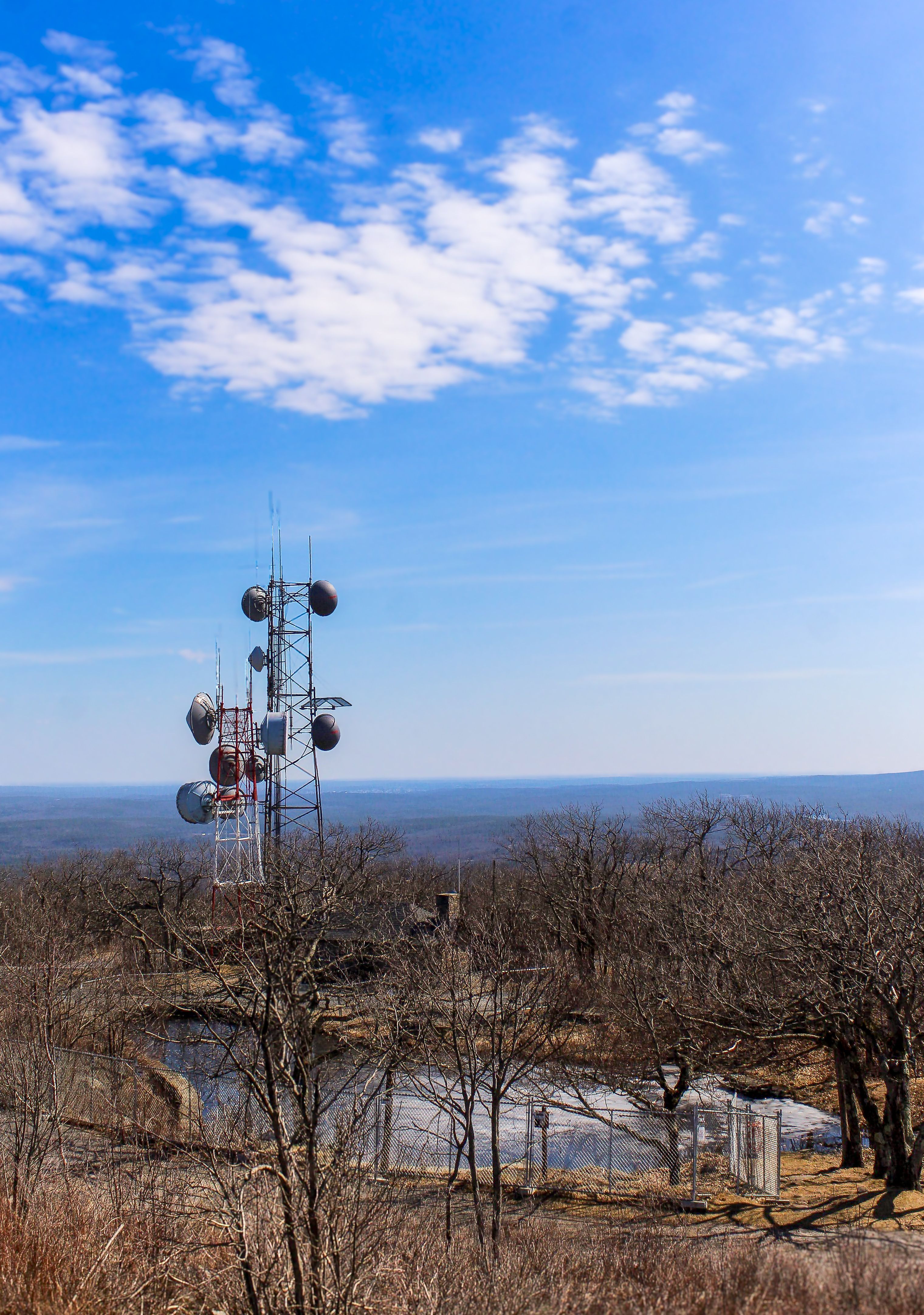 A telecommunication tower stands amidst a serene mountain landscape with barren trees.