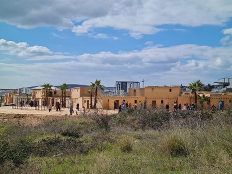 Panoramic view of a desert village with palm trees under a vibrant sky, showcasing traditional architecture.