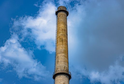 A striking view of a tall industrial chimney against a clear blue sky with clouds.