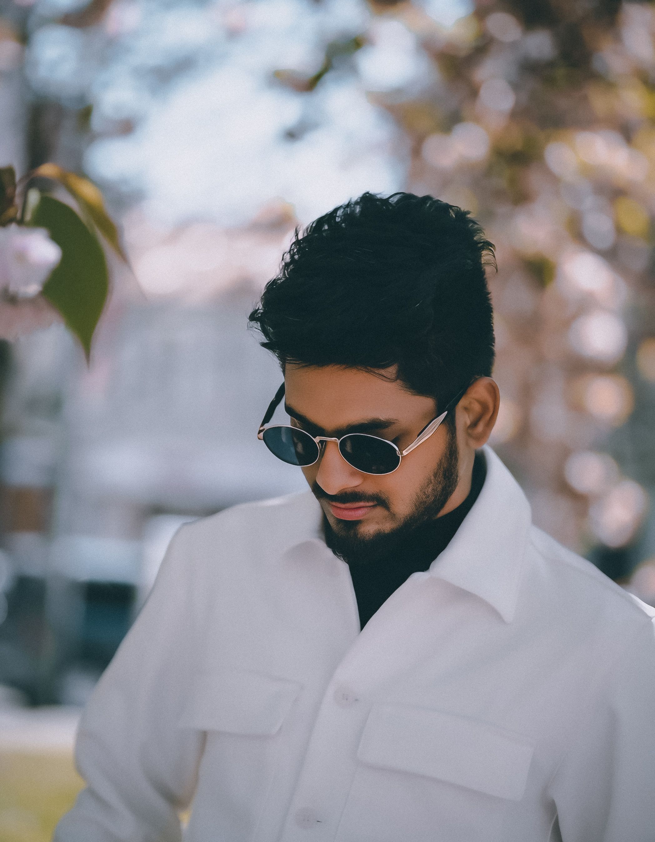 Fashionable man wearing sunglasses and a white jacket, captured in a sunny outdoor setting in Italy.