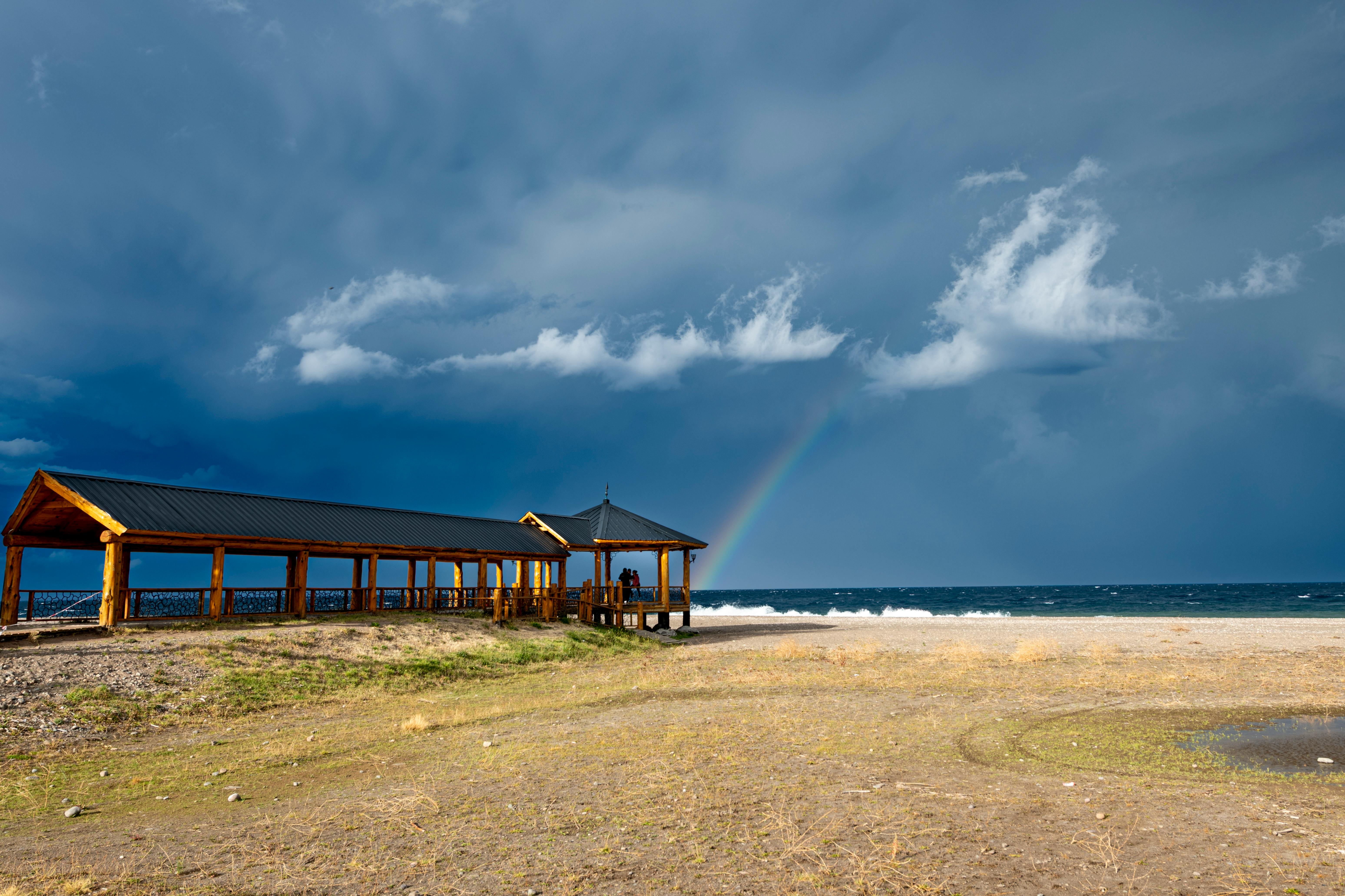 A wooden gazebo by the sea under dramatic skies with a rainbow in Santa Cruz, Argentina.