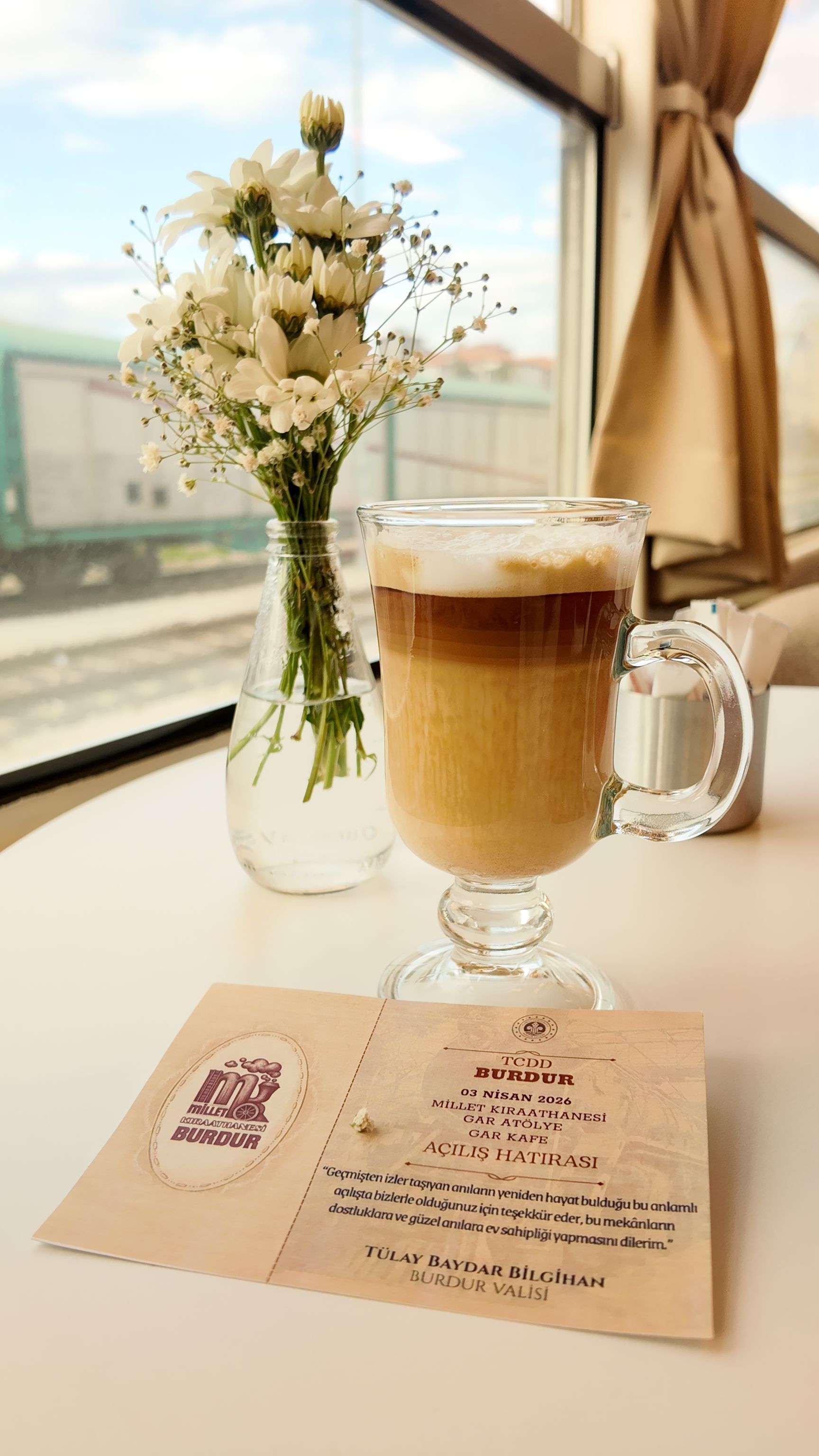 Elegant cafe scene with cappuccino and flowers by the window in Burdur, Türkiye.
