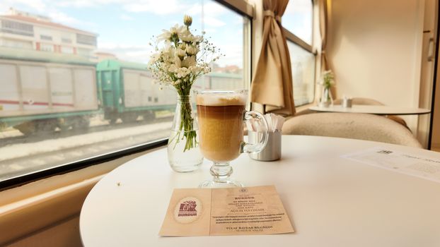 A cozy train cafe in Burdur, Türkiye, featuring a latte and flowers by the window.