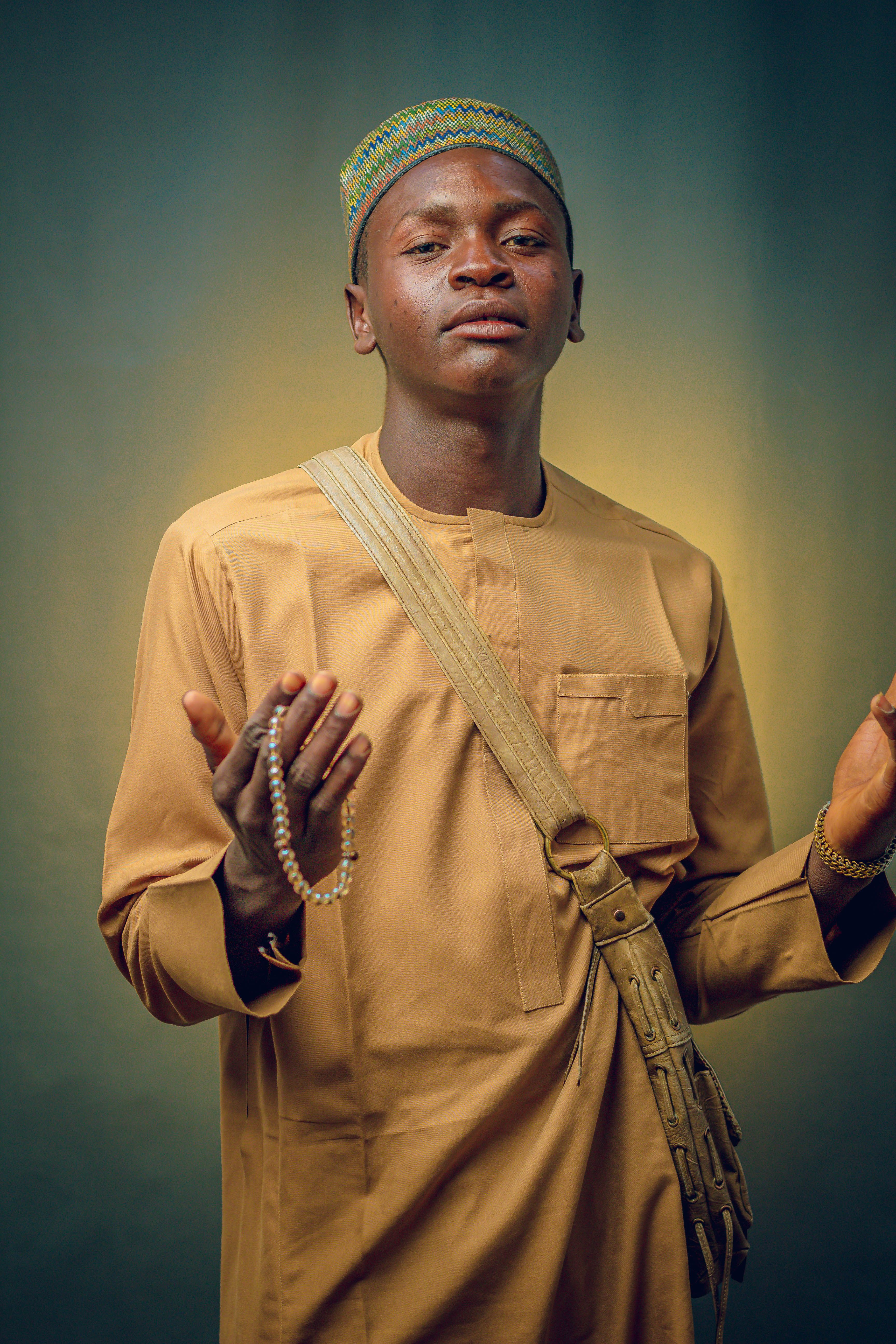 Portrait of a man in traditional attire holding beads against a warm background.