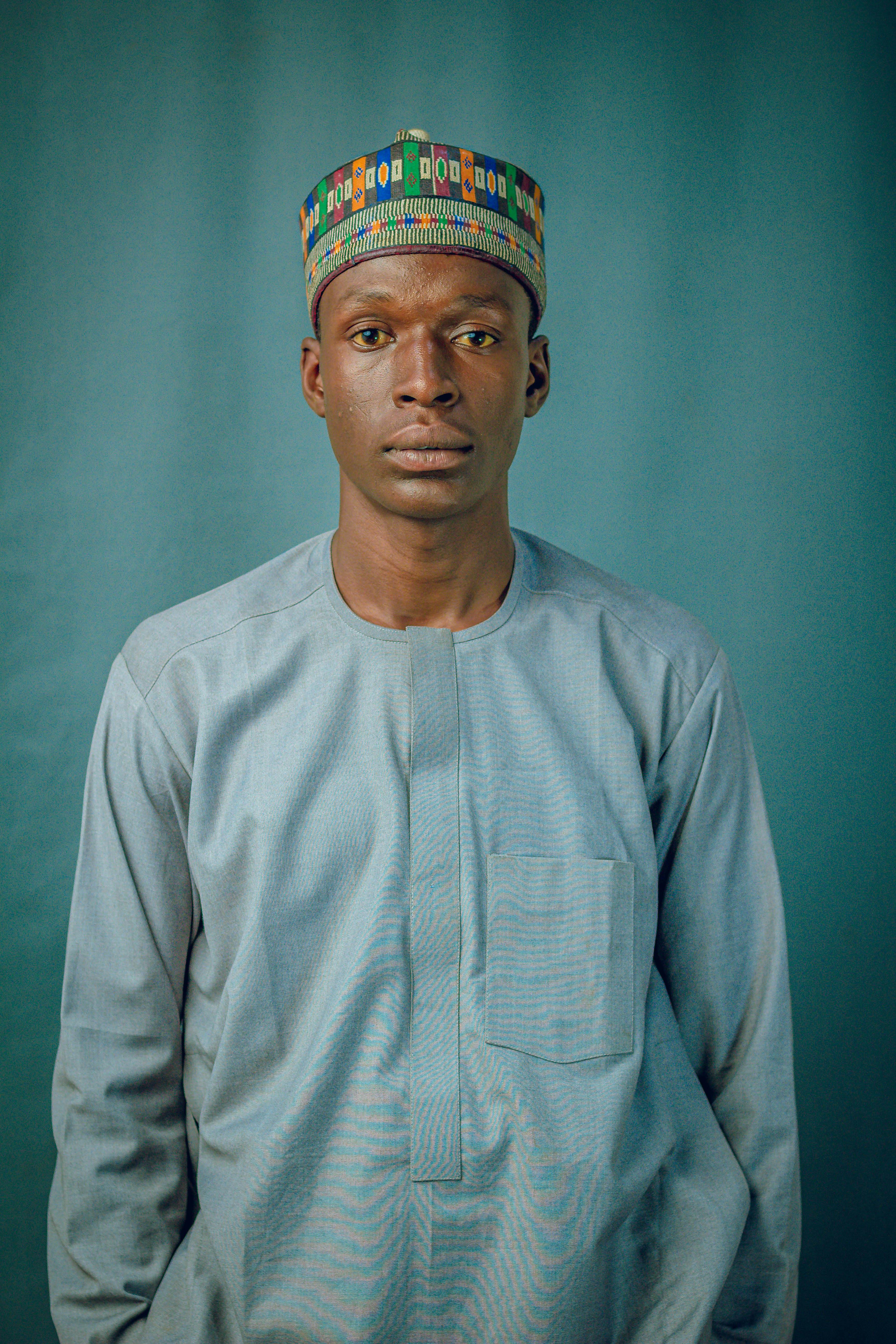 A portrait of a man wearing traditional African attire and a colorful hat against a plain backdrop.