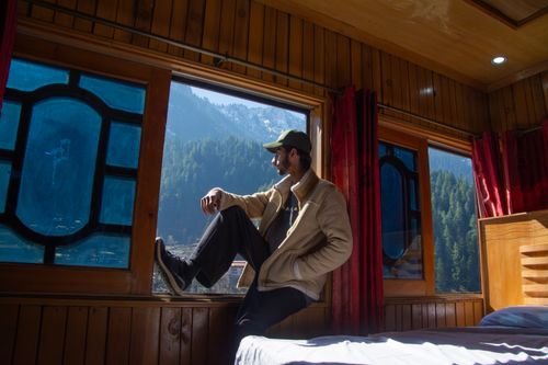 Free Man sitting by window in wooden cabin enjoying breathtaking mountain view, perfect scene for relaxation Stock Photo