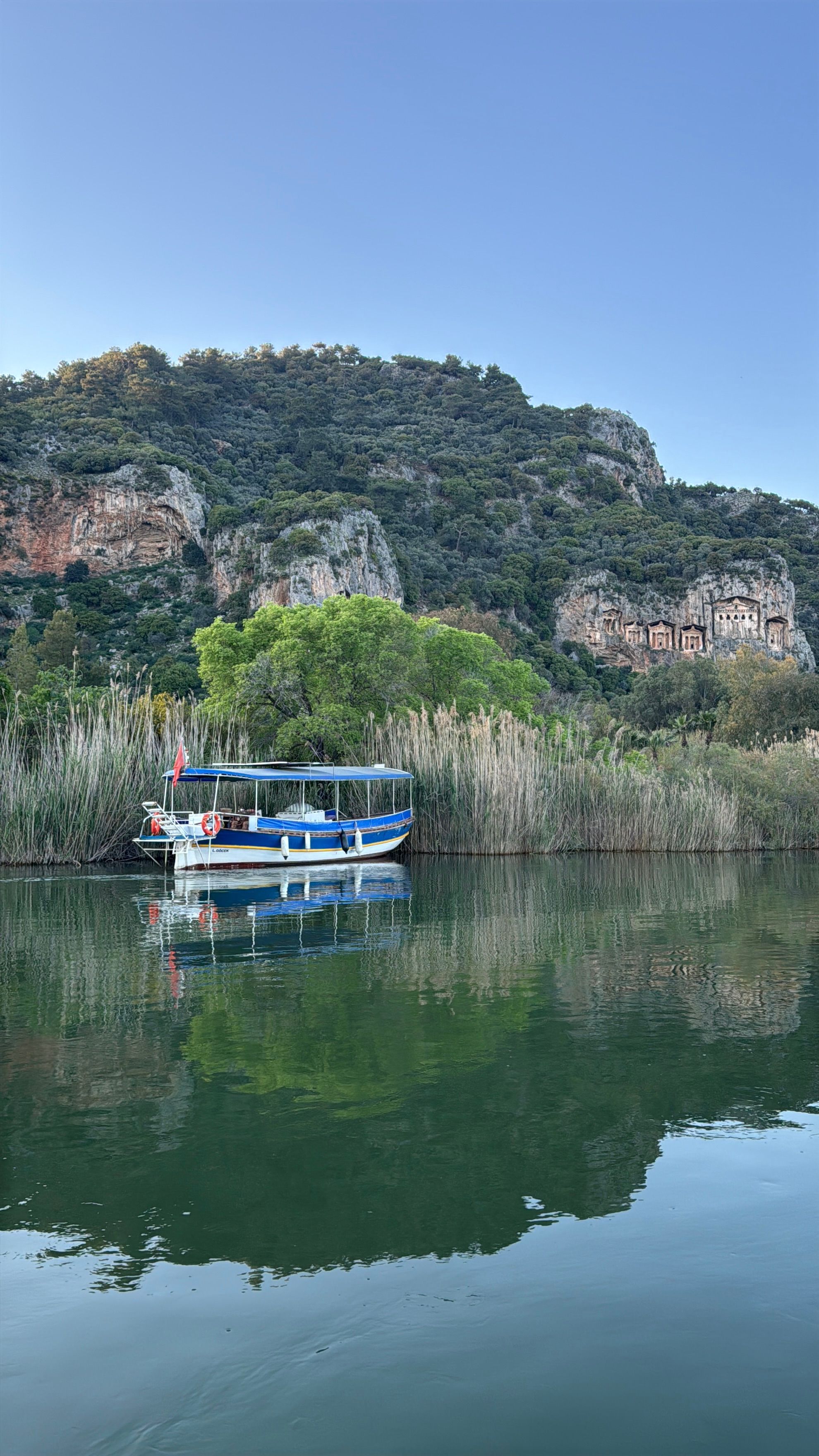 Peaceful view of the Dalyan River reflecting a boat with Lycian tombs in the mountains.