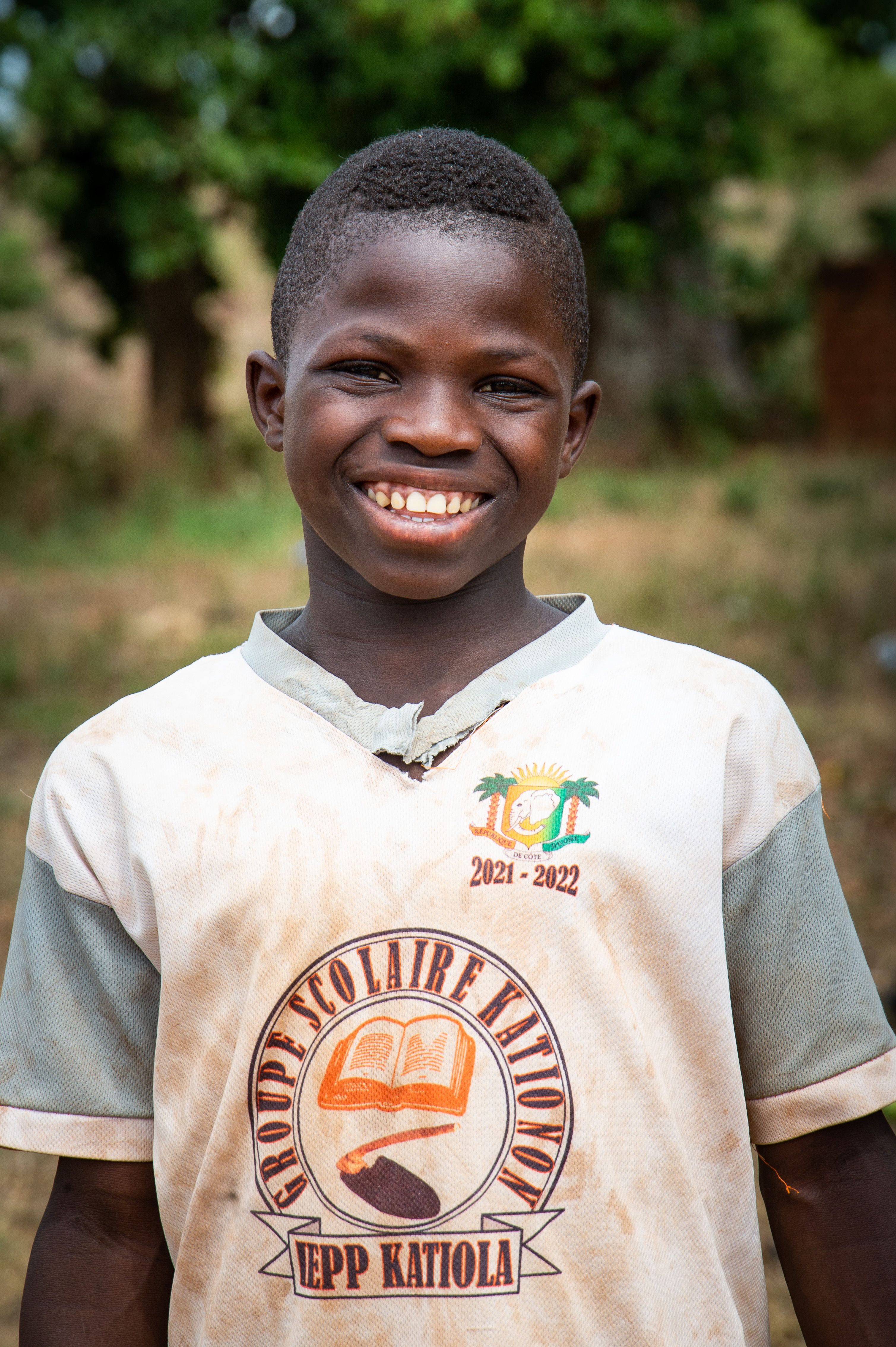 Happy boy wearing a school uniform with EPP Katiola logo, smiling outdoors.