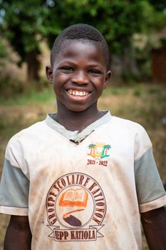 Happy boy wearing a school uniform with EPP Katiola logo, smiling outdoors.