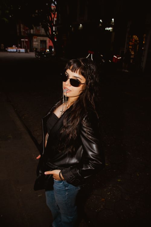 Free Confident woman in sunglasses and leather jacket strolling through city streets at night. Stock Photo