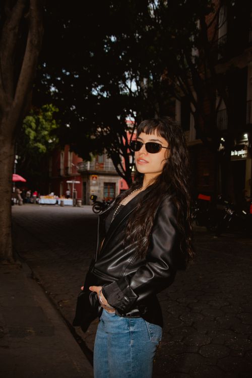 Free Fashionable young woman in sunglasses and leather jacket posing confidently on a vibrant city street Stock Photo