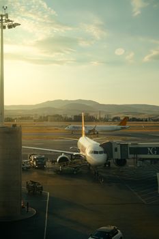 An airplane ready for boarding at an airport terminal with mountains in the background during sunrise.